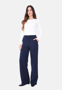 Pantaloni a gamba larga blu navy con una texture liscia, vita alta e tasche frontali. Abbinati a un top aderente bianco a maniche lunghe.