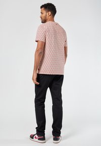 Lyhythihainen punainen ja valkoinen kuviollinen paita rento istuvuus, yhdistetty mustiin housuihin ja punaisilla yksityiskohtilla varustettuihin lenkkareihin, nähtynä takaa.