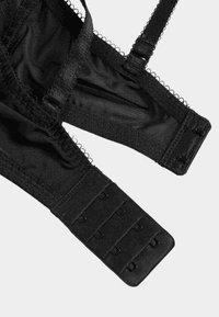 Sort blonder bralette med gennemsigtige meshpaneler, bølget kant, justerbare stropper og lukning bagpå med flere kroge for en sikker pasform.