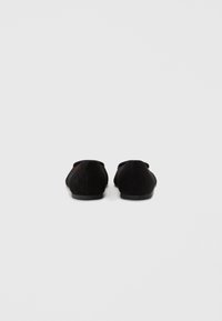 Melni zamšaini čības ar apaļu purngali un zemu papēdi. Dizains ietver minimālas šuves un gludu tekstūru.