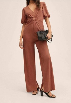 Brązowy kombinezon z głębokim dekoltem w kształcie litery V i krótkimi bufkowatymi rękawami, z centralnym węzłem i rozcięciami na nogawkach, w połączeniu z czarną torbą.