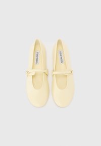 Des ballerines en caoutchouc jaunes avec un bout arrondi, une sangle décorative sur le pied et une texture lisse et brillante.