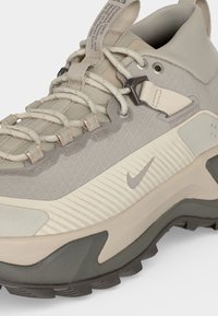 Beige and gray Nike hiking shoe with textured fabric, thick sole, loop laces, metal eyelets, and pull tab on the tongue and heel.
