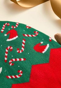 Žalia ir raudona megzta medžiaga su šventiniais raštais, vaizduojančiais Kalėdų senelio skrybėles ir saldainių lazdeles, su baltais akcentais ir tekstūruotu paviršiumi.