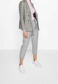 Grijs geruite blazer met dubbele knopen, lichtroze coltrui, grijze cropped broek en witte sneakers. Glad materiaal en perfecte pasvorm.