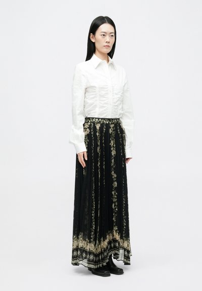 Bijela prilagođena košulja s naborima, uparena s dugom crnom suknjom s cvjetnim uzorcima i višeslojnim rubom. Crne čizme do gležnja.