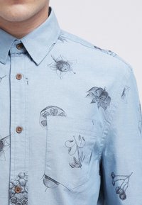 Lichtblauw button-up shirt met een borstzak, met donkere botanische en fruittekeningen die op de stof zijn gedrukt.