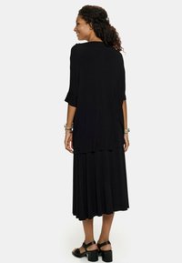 Czarna sukienka do kolan o luźnym kroju, z falbankami i warstwowym designem. Gładki, lekki materiał o eleganckim spłynięciu.