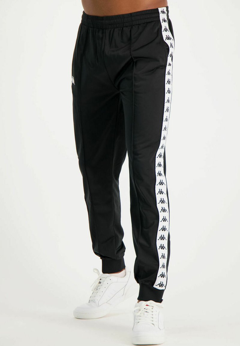 Pantalones de chándal negros hechos de una tela suave y ligera cuentan con rayas laterales blancas con marca. La cintura es elástica para mayor comodidad.
