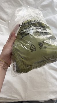 Groen textielartikel verpakt in doorzichtig plastic. Etiket geeft aan dat het voor 80% uit gerecycled materiaal bestaat, bevat recycling-symbool en instructies voor productzorg.