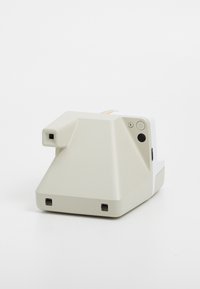 Appareil photo Polaroid en beige clair avec un boîtier texturé, un objectif carré, un bouton d'alimentation et un détail de bande arc-en-ciel sur le dessus.