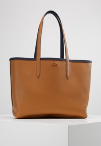 Sac fourre-tout en cuir texturé marron avec des bords noirs et deux anses, arborant un petit logo en relief sur le devant.