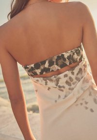 Abito senza spalline con una base di un leggero color crema e un motivo astratto scuro, dettaglio con apertura sul retro e texture liscia.