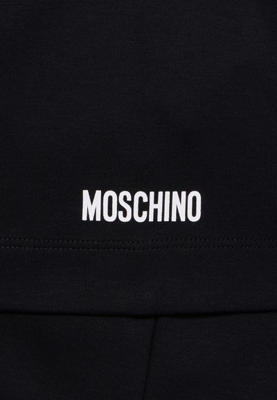 Črna tkanina z belim napisom blagovne znamke "MOSCHINO" natisnjenim nad šivom.