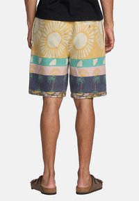 Pantaloni corti multicolori con tessuto testurizzato che presenta motivi di sole e palme. I colori includono giallo, rosa, blu petrolio e blu navy.