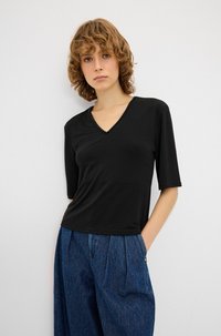 Sort V-hals top med korte ærmer, der har dekorative perler langs halsudskæringen. Sammen med højhalsede blå denimbukser.