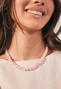 Pink beaded necklace featuring smooth round stones, arranged in a uniform pattern, worn over a light-colored top.