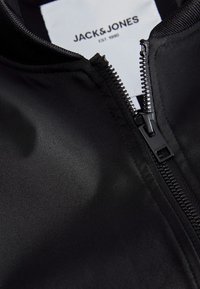 Black Jack & Jones garment with partially open zipper and visible white label showing brand name and establishment year.