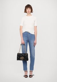 Black quilted handbag with a gold logo, gold chain strap, high-waisted blue jeans, and a fitted white short-sleeve top.