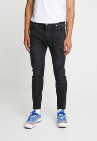 Jeans negros de corte slim con detalles desgastados y cinco bolsillos. Equipados con herrajes en tono dorado. Combinados con zapatillas blancas y azules.