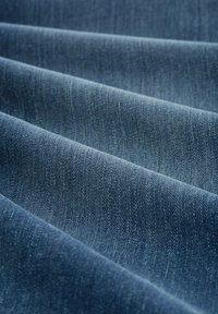 Tissu en denim de couleur bleu foncé avec une surface texturée. Présente un tissage diagonal visible et de subtiles variations de couleur à travers les sections pliées.