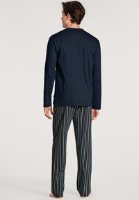 Marineblauw langslavige top met een ronde hals, gecombineerd met gestreepte pyjamabroek in marineblauw, groen en geel. Zachte stof, relaxte pasvorm.
