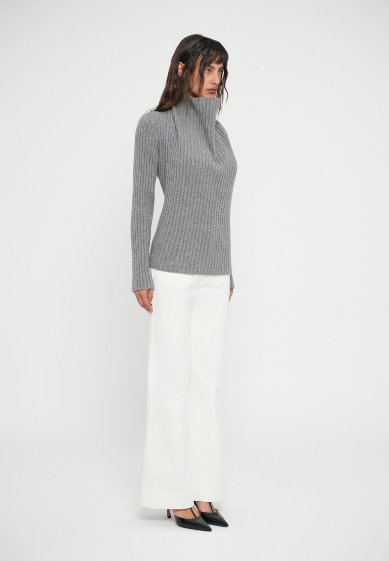 Gray ribbed sweater with a high collar, fitted shape. Paired with white wide-leg trousers and black pointed-toe heels.
