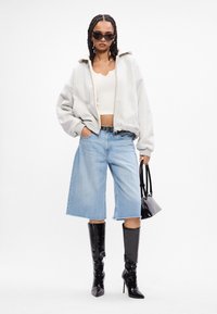 Svijetlo sivi oversized dukserica, bijeli crop top, plave traper Bermuda šortse, crne čizme do koljena i mala crna torbica. Crne sunčane naočale.