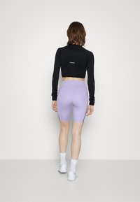 Zwarte lange mouwen crop top met mesh details; lichtpaarse high-waisted fietsbroek met zijstrepen; witte sneakers en sokken.