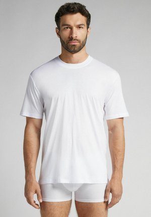 Weißes T-Shirt mit kurzen Ärmeln aus weichem Material, mit einem runden Ausschnitt und einem lockeren Schnitt, getragen über weißen Boxershorts.