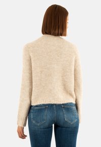 Maglione beige a maglia testurizzata con design corto e polsini a coste, abbinato a jeans in denim blu scuro con tasche posteriori.