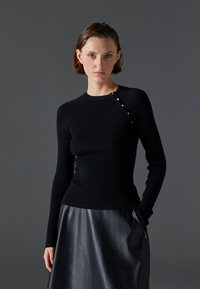 Black ribbed long-sleeve top with a crew neckline and snap-button detail on the shoulder, paired with a black leather skirt.