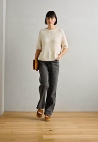 Suéter de punto beige claro con mangas cortas, combinado con pantalones de pierna ancha en gris oscuro y sandalias de plataforma de madera marrones. Los accesorios incluyen un bolso marrón.
