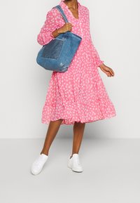 Abito floreale rosa con maniche lunghe e gonna arricciata, abbinato a una borsa a tracolla in denim blu e sneakers bianche.