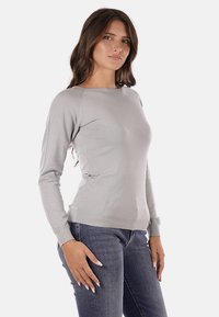 Maglione grigio a maniche lunghe con design aderente, polsini e orlo a coste, realizzato in tessuto liscio. Abbinato a jeans blu scuro.
