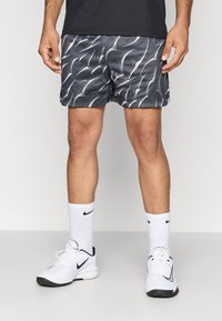 Μαύρο σορτσάκι με κυματιστό λευκό σχέδιο, φτιαγμένο από ελαφρύ ύφασμα. Συνδυασμένο με άσπρες κάλτσες Nike και ασπρόμαυρα αθλητικά παπούτσια.