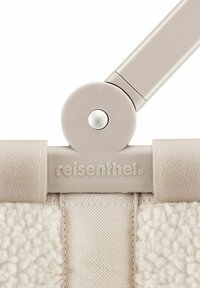 Detail eines Reisenthel Klappstuhls mit einem hellbeigen Metallrahmen, einem plüschigen texturierten Stoff und einer glatten runden Verbindung mit einem metallischen Akzent.