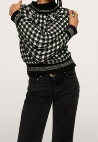 Pull en maille à carreaux noir et blanc avec poignets et ourlet côtelés, associé à un jean noir taille haute avec poches avant et ceinture.