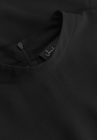 Črna obleka z okroglim izrezom, gladko teksturo in skritim zadrgo na hrbtni strani. Na etiketi je označen naziv blagovne znamke "Vasal."