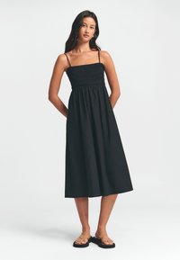 Vestido negro midi con tirantes finos, corsé fruncido y falda fluida. Tejido suave y ligero con una textura sencilla.