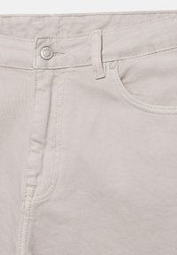 Gros plan sur la ceinture beige clair d’un pantalon montrant le bouton, la boucle de ceinture, la poche avant et les détails des coutures.