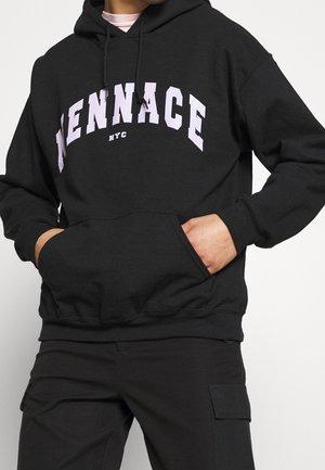 Person wearing black hoodie with "MENNACE NYC" text in large white letters, hands in front pocket, paired with black cargo pants.