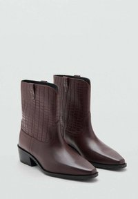 Botas de vaquero burdeos con punta afilada, confeccionadas en cuero liso y con textura de cocodrilo, y un tacón bajo apilado. Acabados de costura sutil.