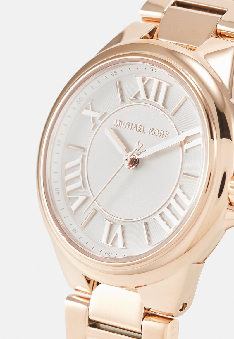 Michael Kors-klocka med ett armband i roséguld och en rund vit urtavla med romerska siffror. Texturerad detaljering omger glaset.