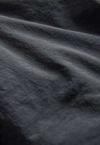 Tessuto grigio scuro strutturato con superficie increspata e leggero splendore, caratterizzato da un aspetto intrecciato leggero e una texture morbida, leggermente stropicciata.