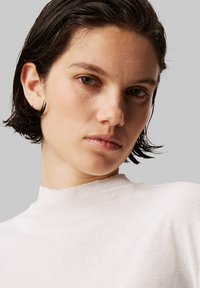 Haut rose clair à col montant en tissu doux et texturé. Le design présente une silhouette ajustée et des lignes épurées, mettant en avant la simplicité.