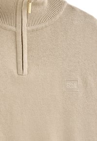 Beżowy sweter z dzianiny z wysokim kołnierzem, z fasonem na pół-zamek. Posiada teksturowaną powierzchnię oraz małe logo "POLO CLUB" wyszyte z przodu.