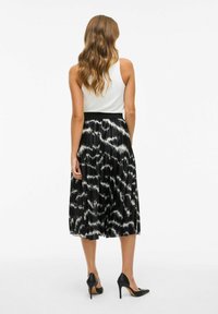 Svart og hvit plisse midi-skjørt med et dristig mønster, kombinert med en tettsittende hvit tanktop og svarte høye hæler.