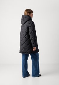 Zwarte gewatteerde pufferjas met een hoodie, met een iets oversized pasvorm, diamanten patroon en een knielange snit. Gepaard met wijde spijkerbroeken.