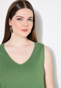 Groene mouwloze top met een V-halsontwerp. Gemaakt van lichtgewicht stof, met een soepele textuur en nette stiksels langs de halslijn.